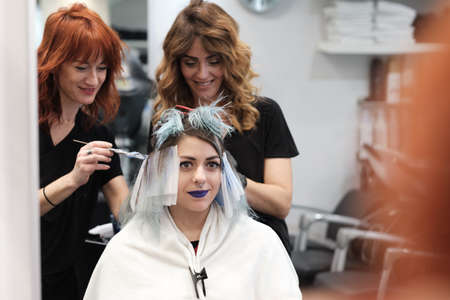 two young hairdresser dyeing hair of female client while she sitting in chairの写真素材