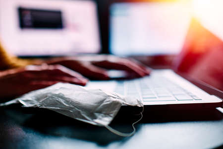 a closeup image of a woman working and typing on laptop computer keyboard with a mask during coronavirus crisisの写真素材