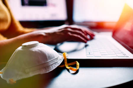 a closeup image of a woman working and typing on laptop computer keyboard with a mask during coronavirus crisisの写真素材