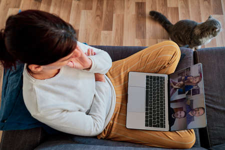 a woman at home using laptop to video conference with friends during coronavirus pandemic - social...