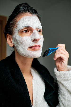 woman using facial mask with brush and towelsの写真素材