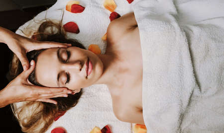 Relaxed woman lying on spa bed for facial and head massage spa treatment by massage therapist in a luxury spa resort. Wellness, stress relief and rejuvenation conceptの写真素材