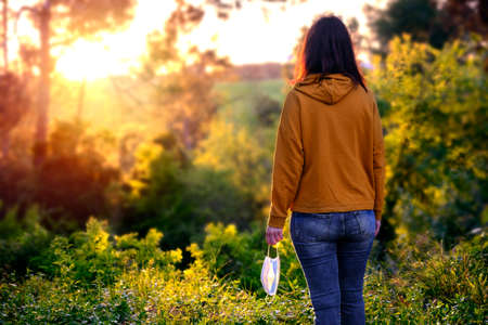 woman looks to the future in a natural place with face mask in her hands - social distancing conceptの写真素材