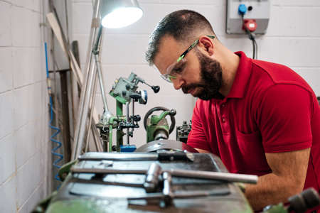 Closeup worker in uniform and protective glasses working on sharpening machine toolの写真素材