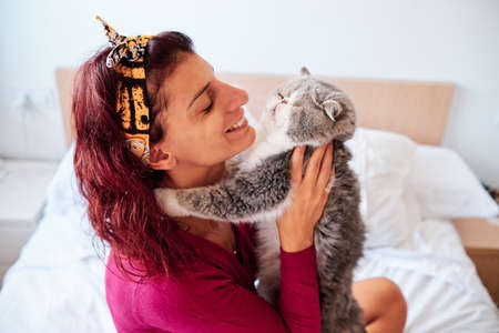 happy woman with her exotic cat in her bedroom - pet care concept