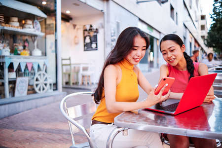 two asian women using a computer outdoorの写真素材