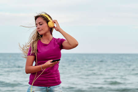 young woman at the beach hearing music with yellow headphonesの写真素材