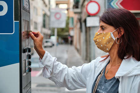adult woman with mask insert coins in park meter