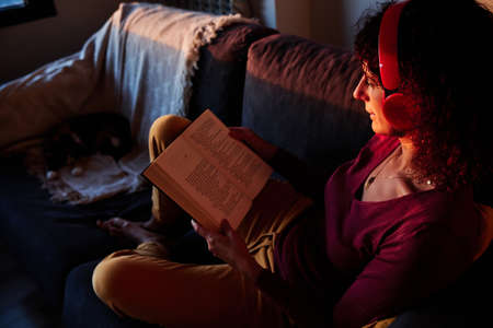 woman reading a book on couch during quarantine for coronavirus - stay at home concept