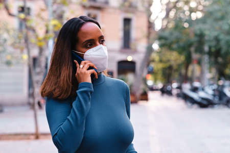 black woman with protective mask using a smartphone - new normalの写真素材