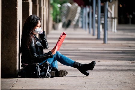 Woman wearing a face mask and using a digital tablet outdoors.の写真素材