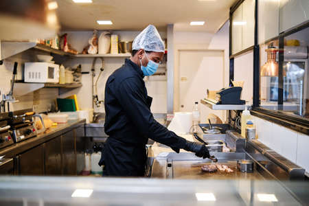 Close-up of professional latin chef man wearing a protective mask and uniform while working at restaurant kitchen.の写真素材