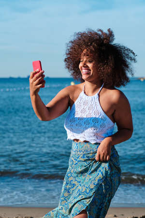 young curvy woman dancing with smartphone for viral video at the beach