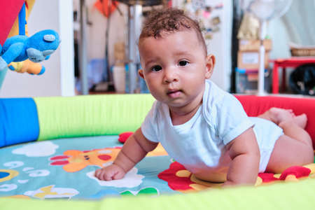 Baby lying on a colorful play mat on the floor at home.の写真素材