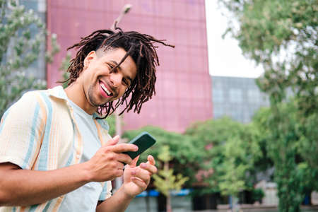 a confident young man with curly hair using smarpthone and looking at camera