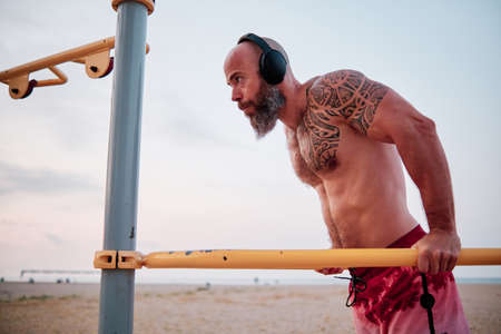 Athlete man practicing calisthenics while doing chin-ups at the beach.