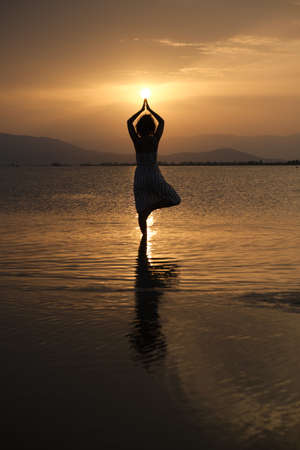 Silhouette of a woman practicing yoga during the sunset.