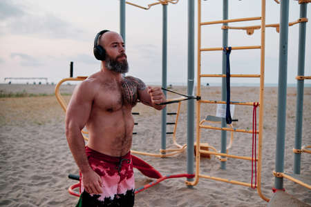 Athlete man exercising with elastic band during calisthenics workout at the beach.