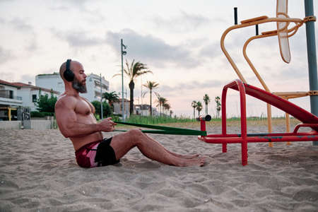Sportive man doing calisthenics workout with a resistance band at the beach.