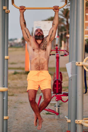 Athletic man doing pull up exercise during calisthenic workout training outdoors.