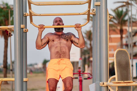 Fitness man performing pull-up exercise during calisthenics workout outdoors.