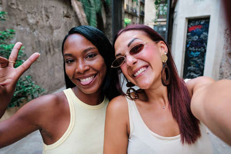 Young female friends having fun while taking selfies together outdoors.