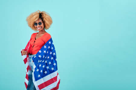 Smiling afro woman holding an USA flag while standing on an isolated background.の写真素材