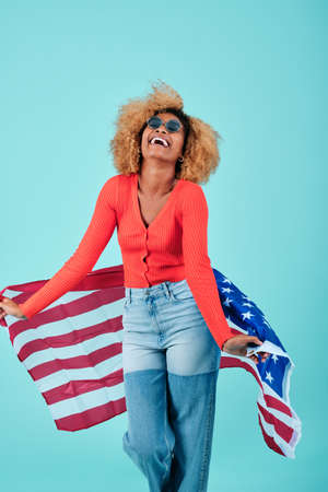 Cheerful afro woman holding a USA flag while celebrating Independence Day.の写真素材