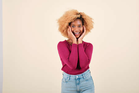 Happy afro woman looking surprised at the camera while posing against an isolated background.の写真素材