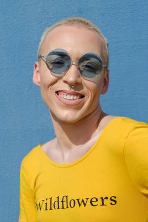 Close up view of a young non-binary person wearing sunglasses and smiling while posing outdoors.