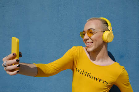 Non-binary person smiling while taking selfies with a mobile phone outdoors.の写真素材