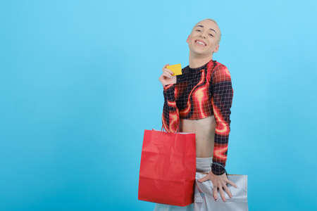 Non-binary person smiling while holding a credit card and shopping bags over an isolated background.の写真素材