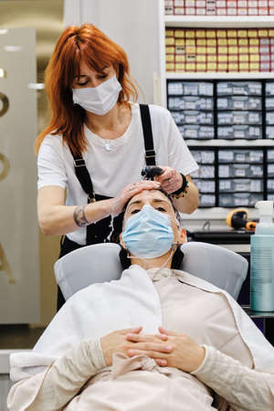 A hairdresser and her client wear face masks during hair wash in the beauty salon.の写真素材
