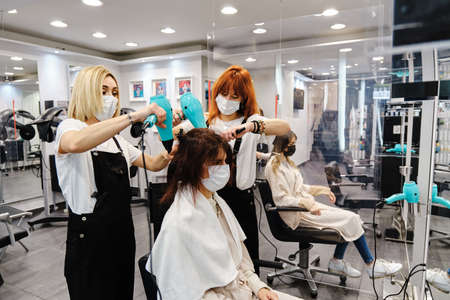 Two professional stylists drying and styling the hair of a client in the hair salon.の写真素材