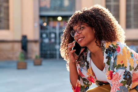 young afro american woman with curly hair using her mobile phone outdoorsの写真素材