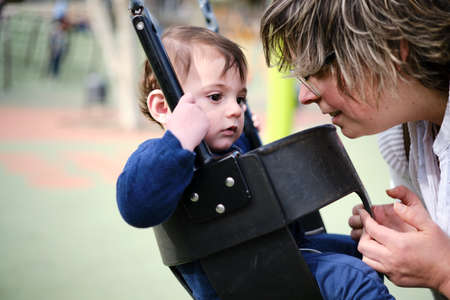 Mother swinging her little son on the swing in the park.の写真素材