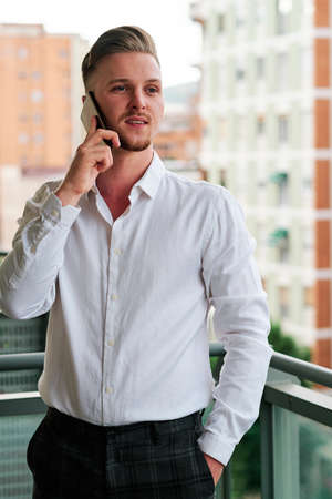 Young executive man talking on the mobile phone while standing on a balcony.