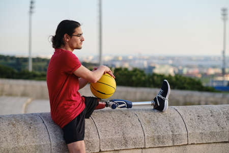 Young man with disability holding a basketball while relaxing outdoors after training.