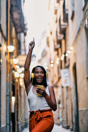 Happy woman dancing while enjoying listening to music with mobile phone and headphones outdoors.
