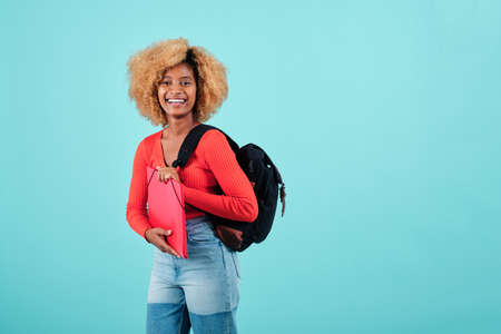 Afro student woman smiling while carrying backpack and holding a folder on an isolated background.の写真素材