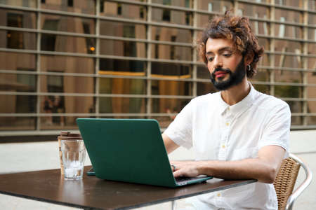 Businessman with makeup working on laptop while sitting in outdoor cafe.の写真素材
