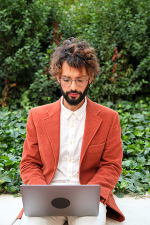 Stylish businessman with glasses working with laptop while sitting outdoors.の写真素材