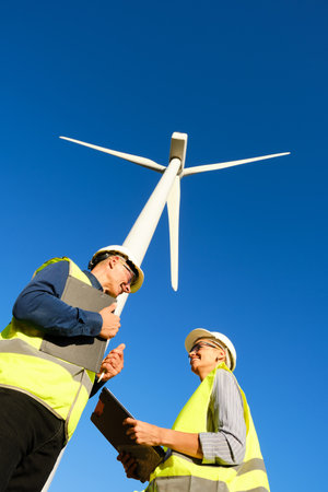 Low angle view of two workers talking while working in a wind turbine field.の写真素材