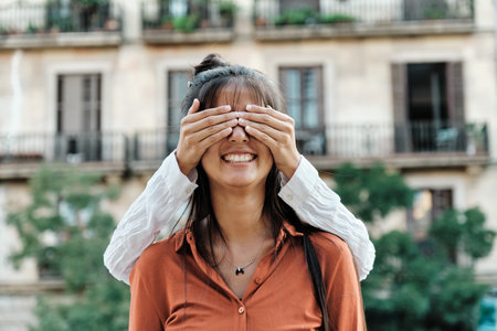 Woman covering her friends eyes while surprising her outdoors on the street.の写真素材