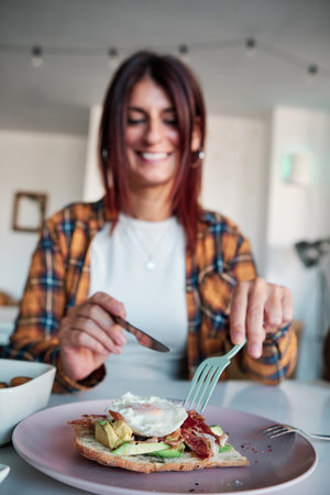 Woman smiling while eating an avocado toast in a cafe or restaurant.の写真素材