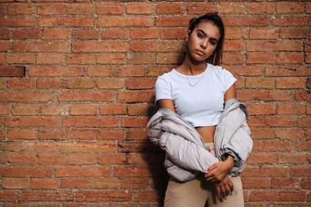 Young woman looking at the camera while posing against a brick wall.の写真素材