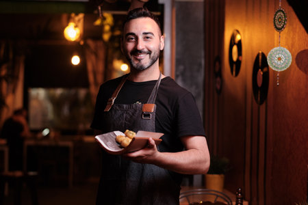 Waiter looking at the camera and smiling while holding a plate with meal in a restaurant.の写真素材