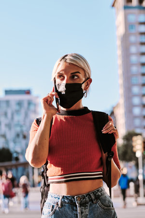 Woman with face mask talking on the phone while walking on the street.