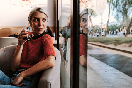 Woman looking out window while drinking a beverage in a restaurant.