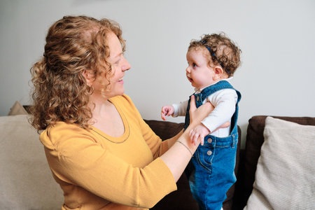 Woman holding and looking at her little daughter while sitting on sofa at home.